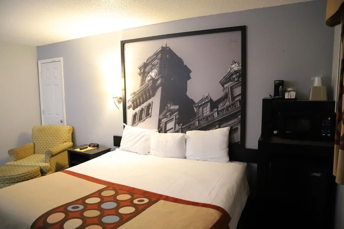 A hotel room with a bed, a chair, a nightstand, a television, and a wall-mounted picture.