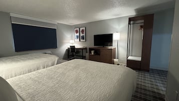 Une chambre d’hôtel avec deux lits, un bureau avec une chaise, une télévision et une lampe.
