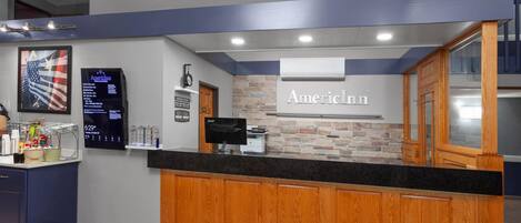A reception area with a wooden counter, a digital display, and a sign that reads "AmericInn."