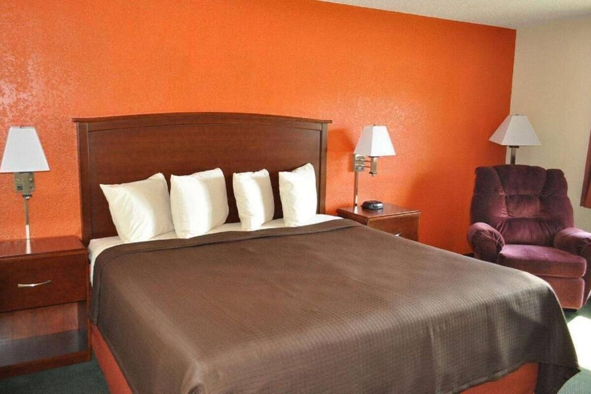A hotel room with a large bed, two bedside tables, a chair, and two wall lamps.