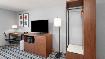 Habitación de hotel con escritorio de madera, televisor de pantalla plana, microondas, lámpara, silla y armario.