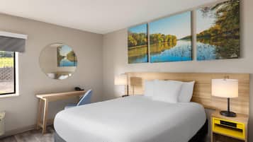 A hotel room with a large bed, a desk, a chair, a round mirror, and two bedside tables with lamps.
