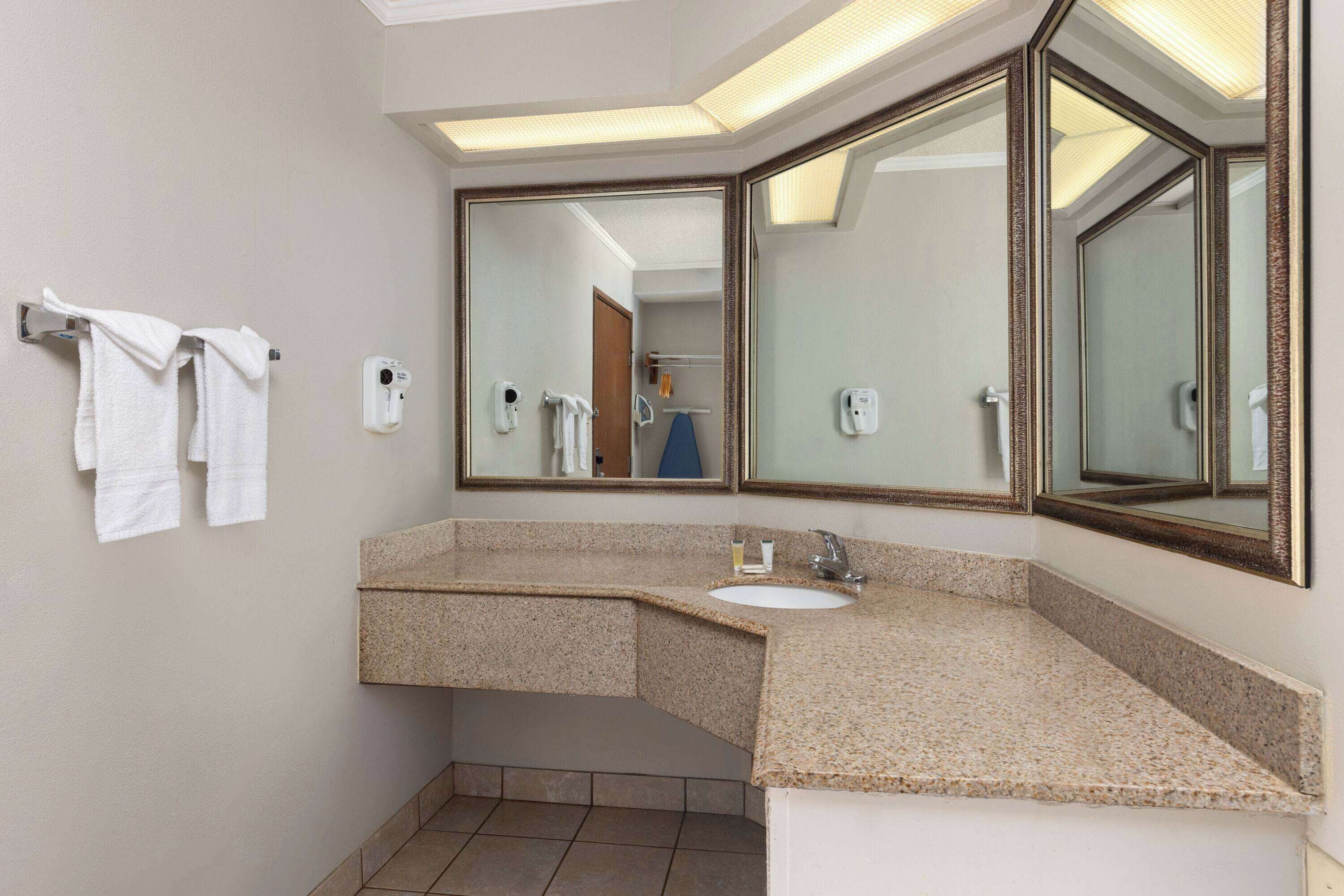 A bathroom with a granite countertop sink, two towel racks, and large mirrors.