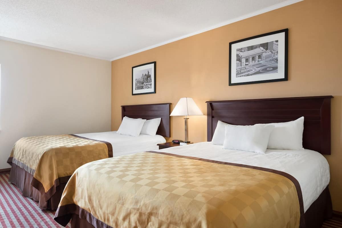 Habitació d'hotel amb dos llits, un terra de pissos quadriculats, una làmpada i quadres a la paret.