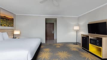 A hotel room with a bed, a flat-screen TV, a minibar, and a ceiling fan.