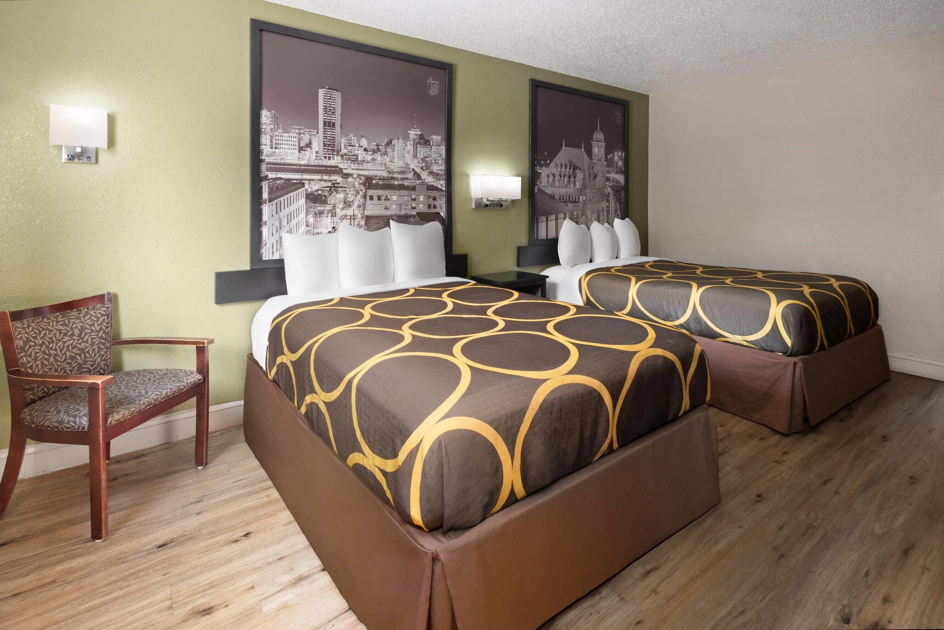 A hotel room with two beds, a chair, and two wall-mounted lamps.