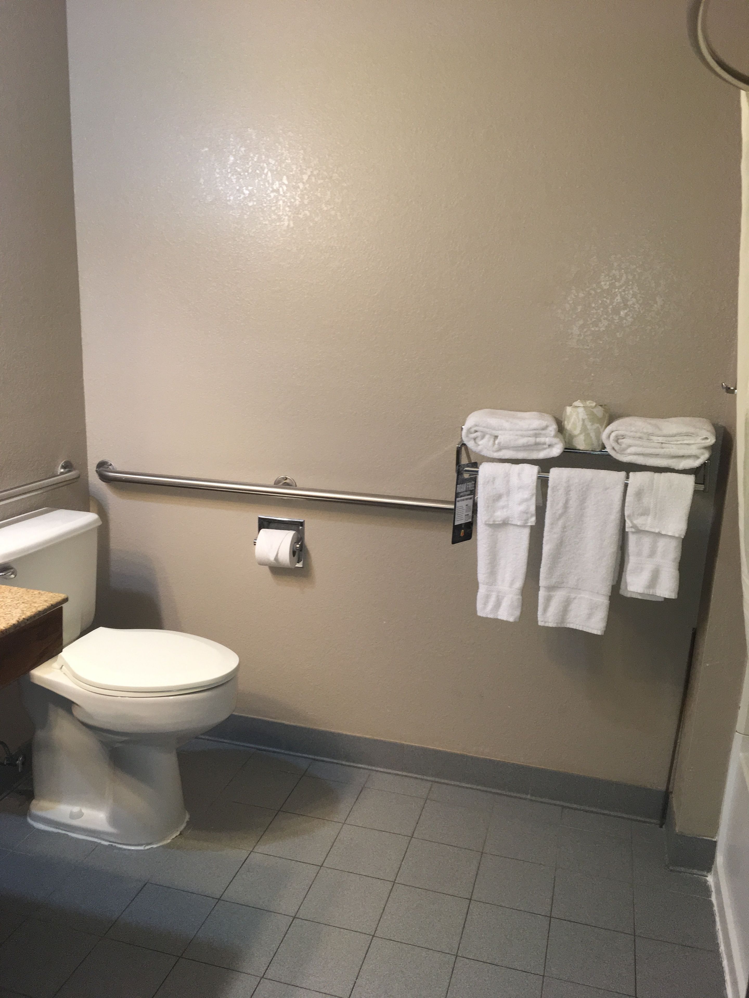 A small bathroom with a toilet, a towel rack with folded towels, and a paper towel dispenser.