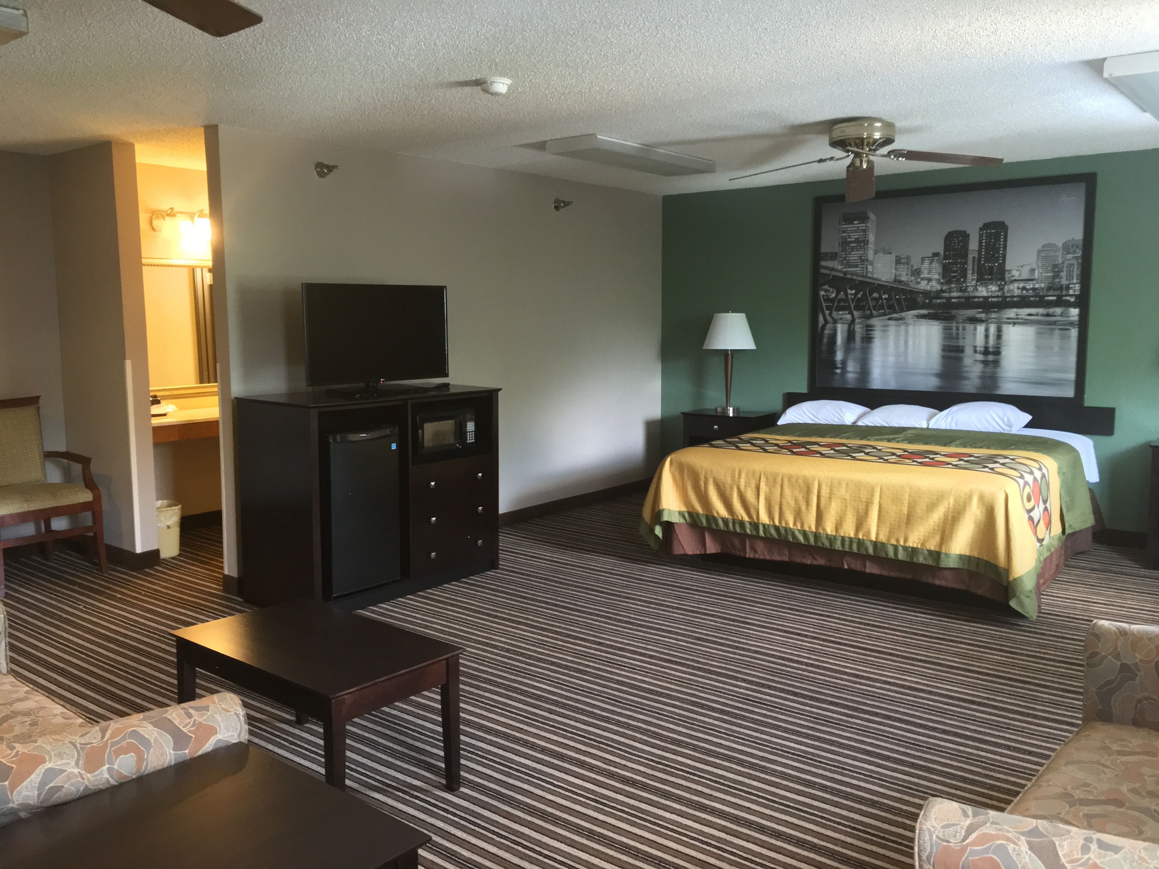 Una habitación de hotel con cama, escritorio, televisor, lámpara y ventilador de techo.