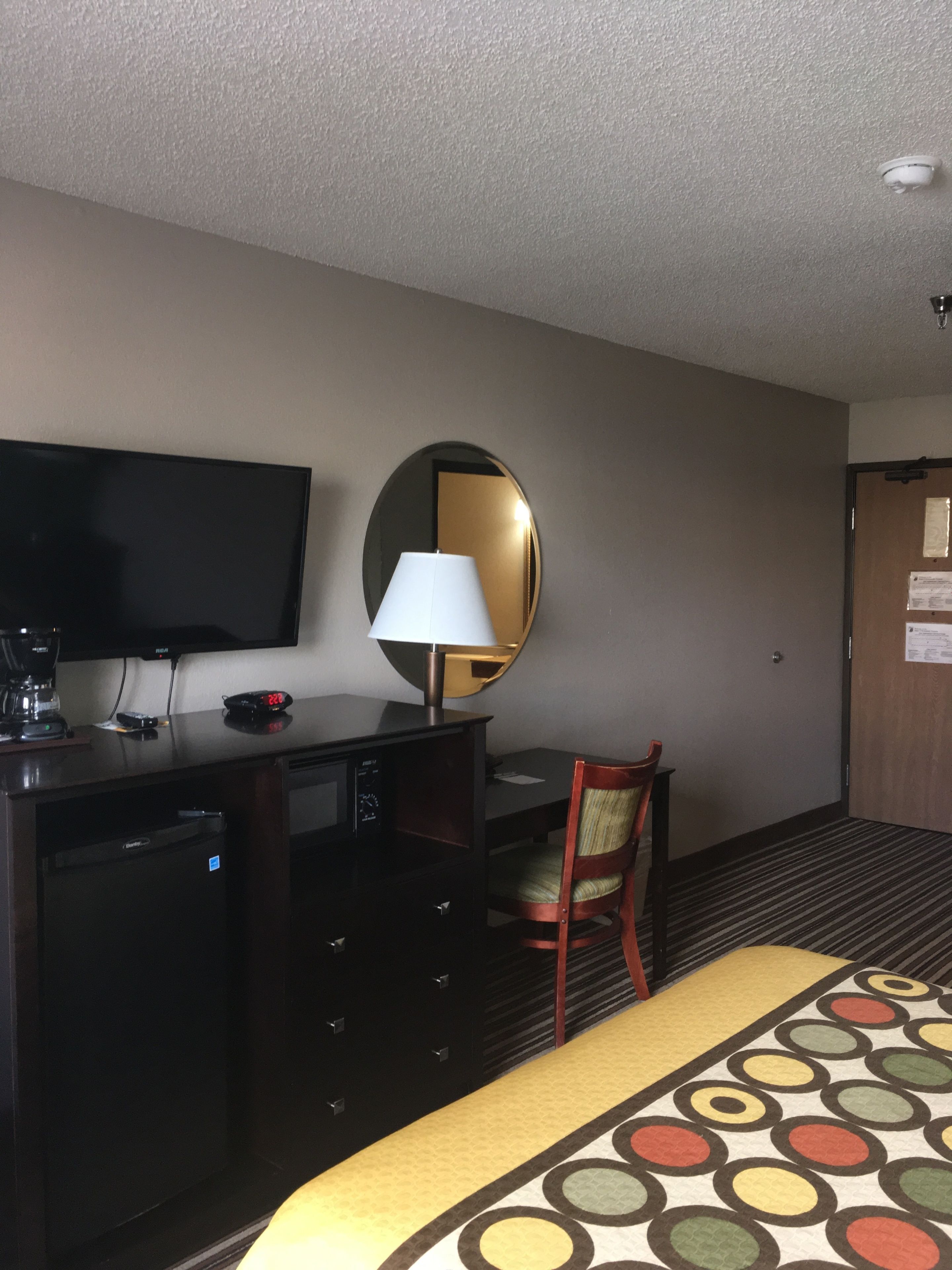 A hotel room with a bed, a desk with a lamp, a television, and a mirror.