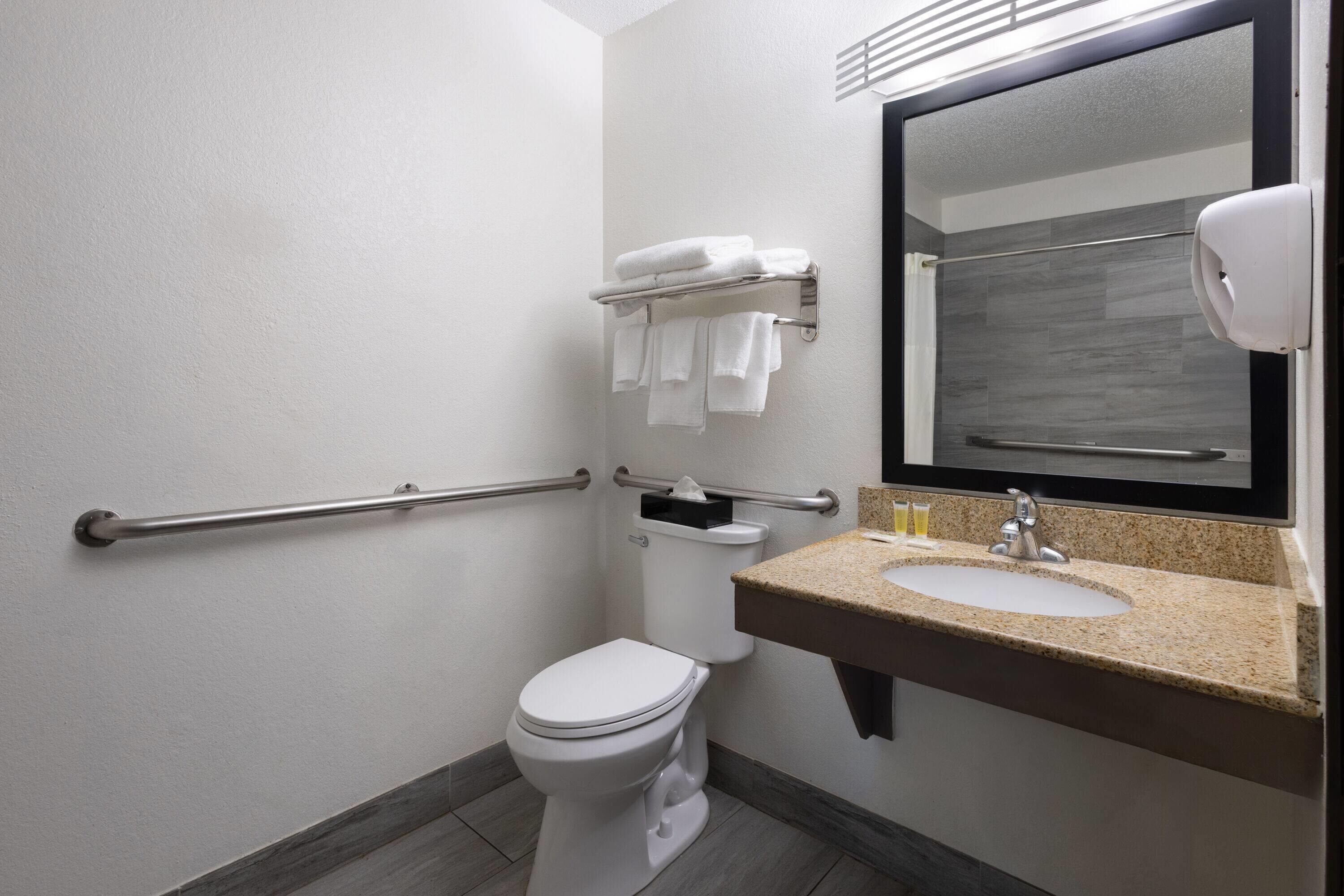 Une salle de bain avec des toilettes blanches, un lavabo doté d’un plan de travail en granit, un porte-serviettes avec des serviettes pliées et un sèche-mains.