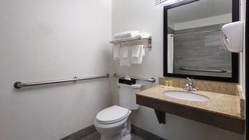 Une salle de bain avec des toilettes blanches, un lavabo doté d’un plan de travail en granit, un porte-serviettes avec des serviettes pliées et un sèche-mains.