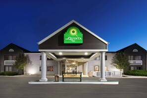 Een La Quinta Inn met een opvallend groen bord, een overdekte ingang en een bank ervoor.