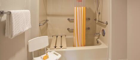 A bathroom with a white bathtub, a shower with a yellow and white striped shower curtain, a white chair with a towel, and a white towel hanging on the wall.