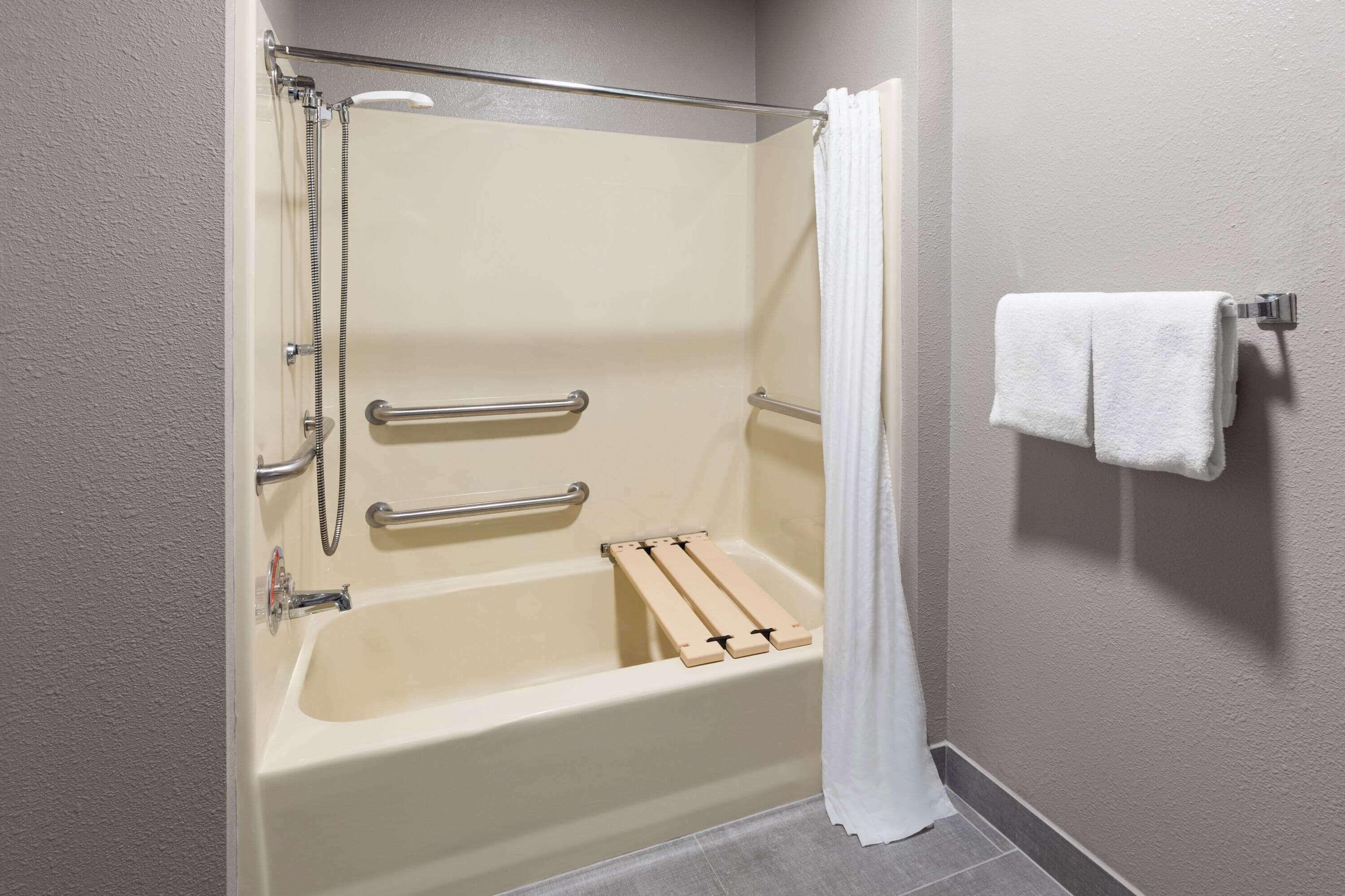 A standard hotel bathroom with a bathtub, shower, and handrails.