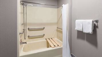 A standard hotel bathroom with a bathtub, shower, and handrails.
