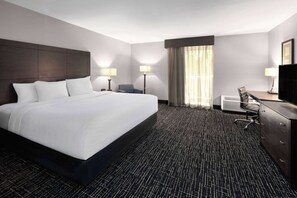 Een hotelkamer met een groot bed, een bureau, een stoel, een televisie en een raam met gordijnen.