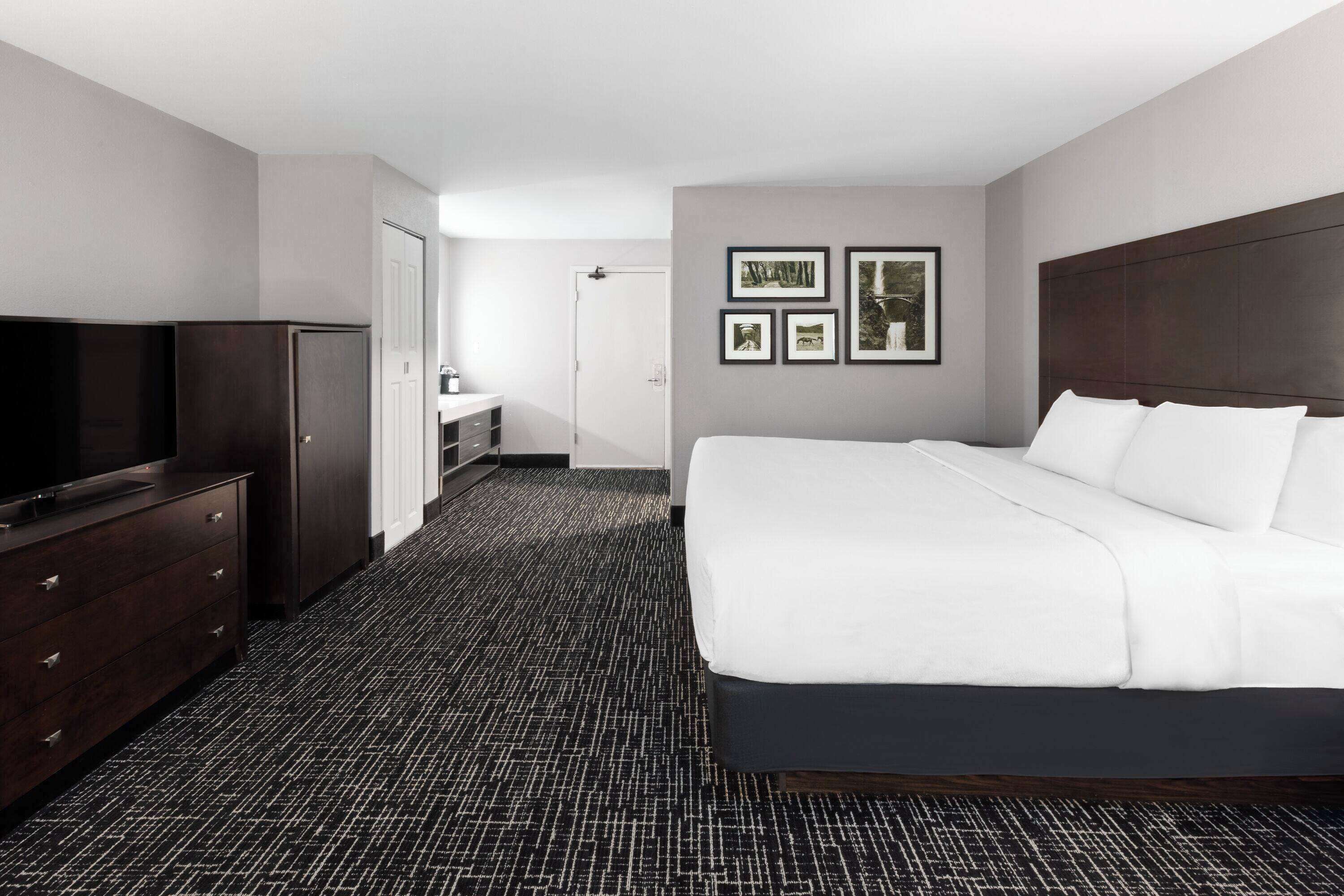 A hotel room with a large bed, a dresser, a television, and framed pictures on the wall.