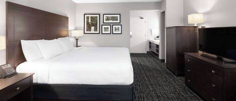 A hotel room with a large bed, a desk with a telephone, a dresser with a television, and framed pictures on the wall.