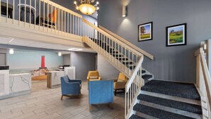 A hotel lobby with a staircase, seating area, and a reception desk. - La Quinta Inn by Wyndham Sheboygan (Sheboygan)