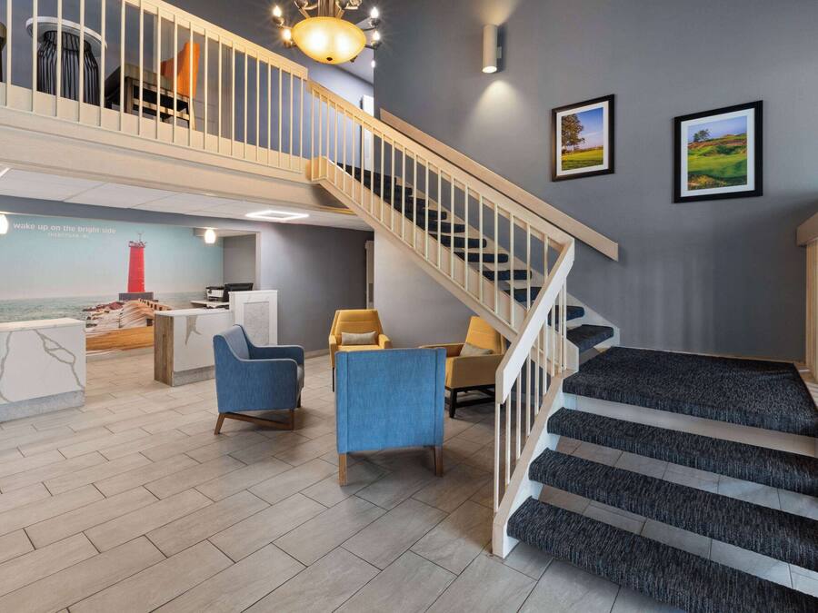 Un vestíbulo de hotel con una escalera, un área de descanso y una recepción.