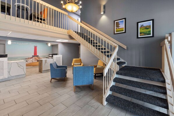 A hotel lobby with a staircase, seating area, and a reception desk. - La Quinta Inn by Wyndham Sheboygan (Sheboygan)