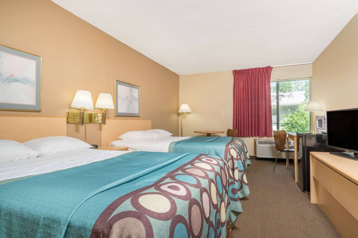 Habitación de hotel con dos camas, un escritorio, un televisor y una ventana con cortinas.