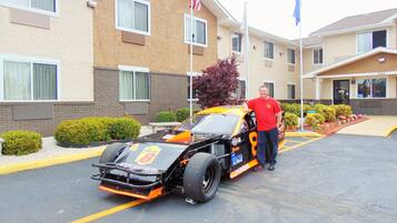 A man standing next to a race car in a parking lot with a building in the background.