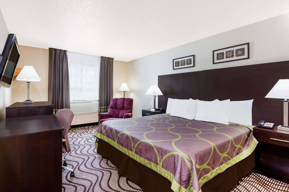 A hotel room with a bed, a desk, a chair, a TV, and a window with curtains.