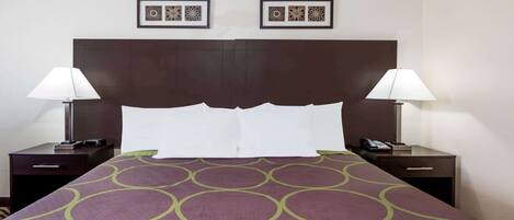 Une chambre d’hôtel avec un grand lit, deux tables de chevet avec des lampes, une tête de lit et deux tableaux encadrés au mur.
