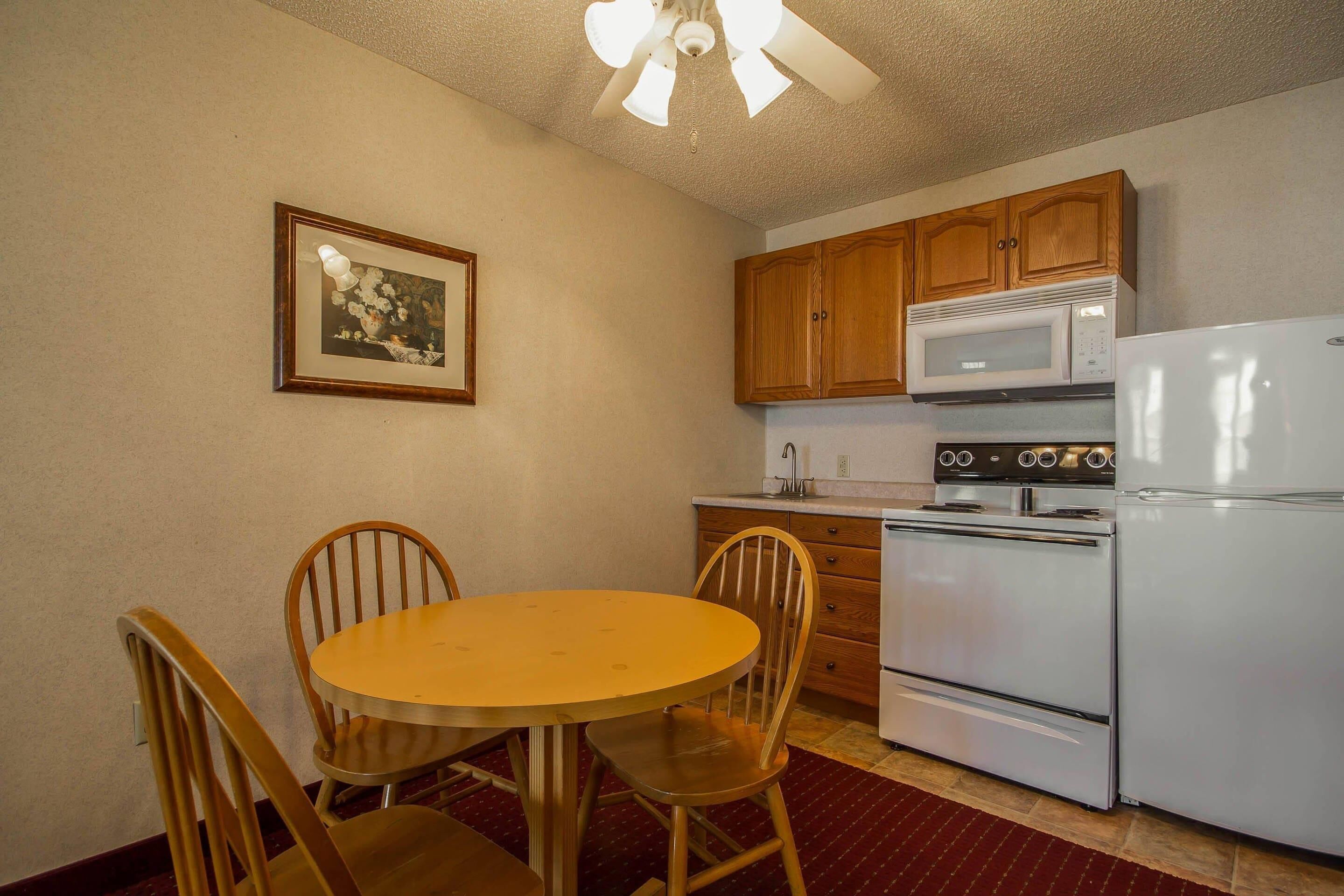 A kitchen with wooden cabinets, a white refrigerator, a stove, and a dining table with chairs.