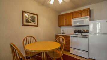 A kitchen with wooden cabinets, a white refrigerator, a stove, and a dining table with chairs.