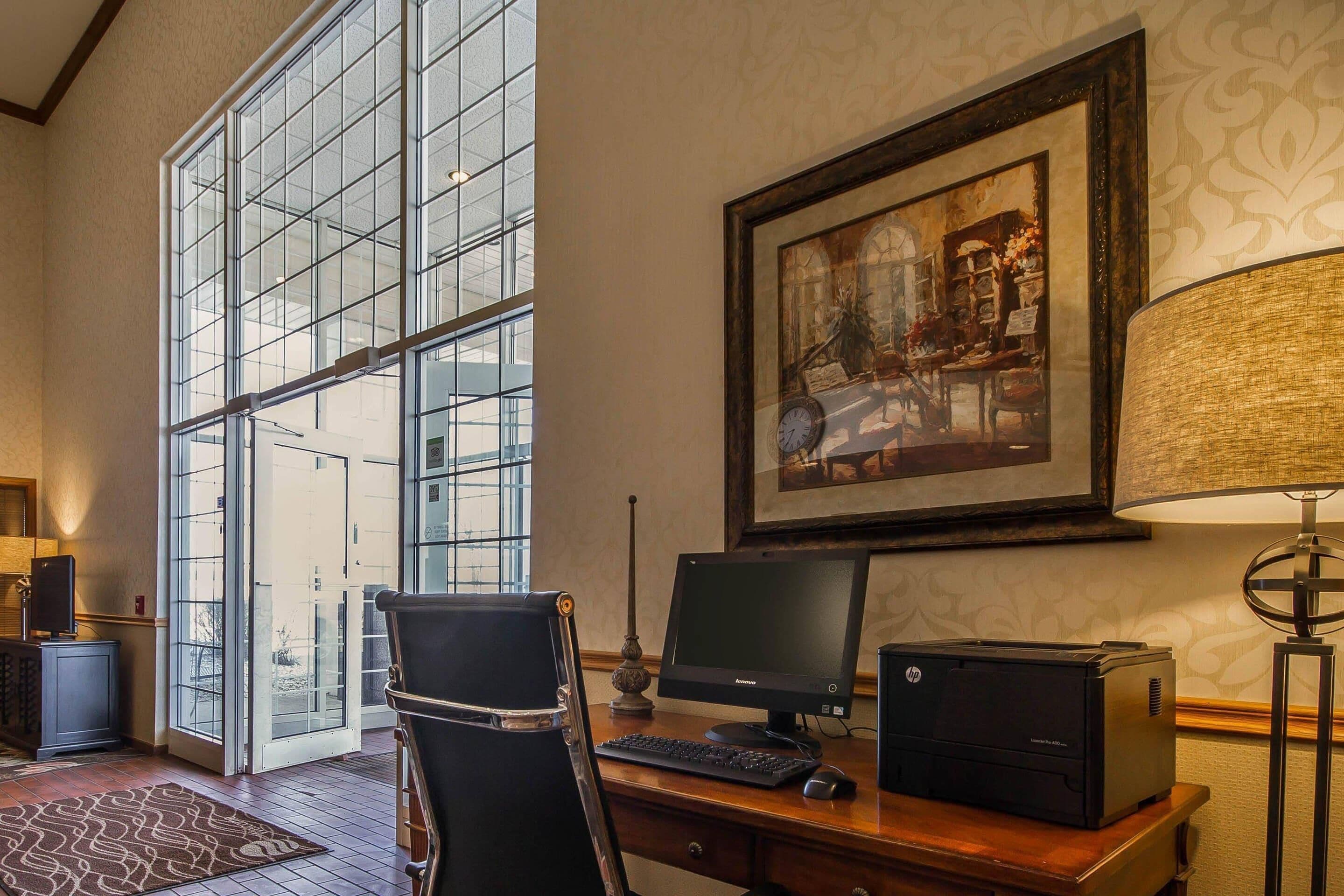 A spacious room with a large window, a desk with a computer, a printer, and a chair.