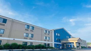 Un hotel de varios pisos con fachada azul y color beige, con un vestíbulo visible y estacionamiento.