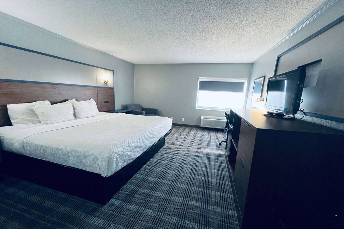 Ein Hotelzimmer mit einem großen Bett, einem Schreibtisch mit Computer, einem Fernseher und einem Fenster.