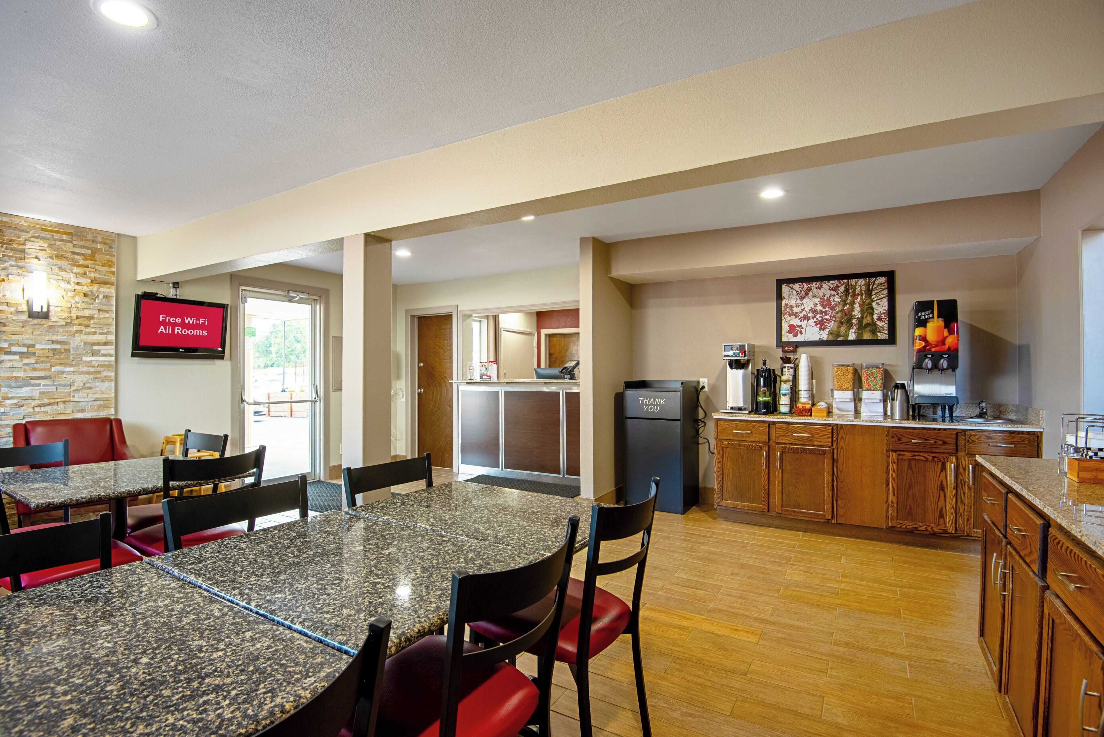A hotel room with a dining area, kitchenette, and a TV displaying 'Free Wi-Fi All Rooms'.