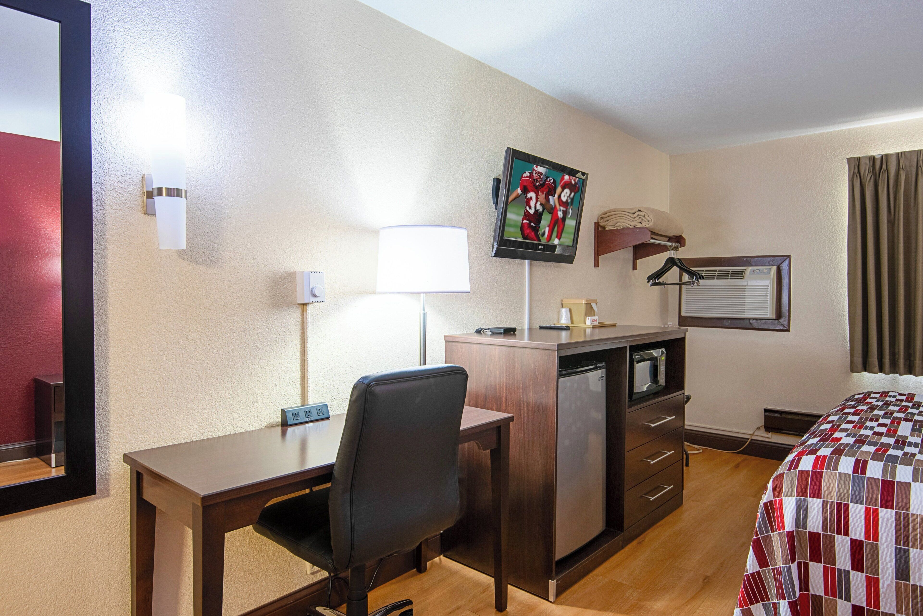 A hotel room with a desk, chair, bed, TV, and a microwave.