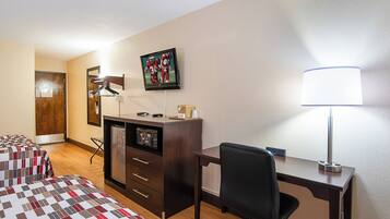 A hotel room with a bed, desk, chair, lamp, TV, and a microwave.