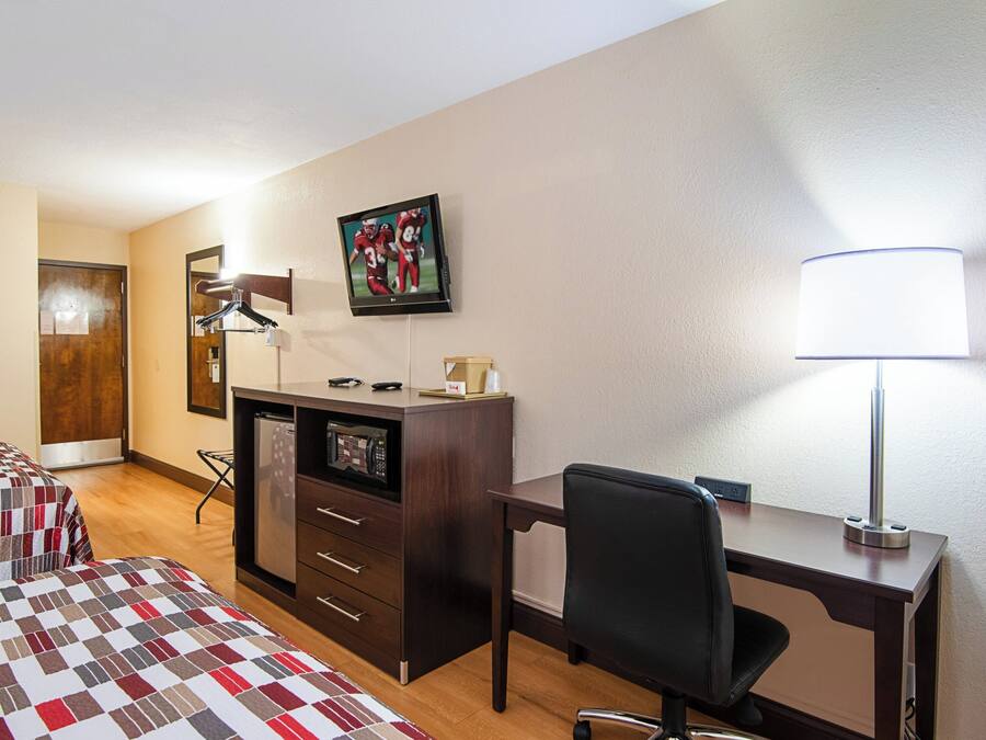 A hotel room with a bed, desk, chair, lamp, TV, and a microwave.