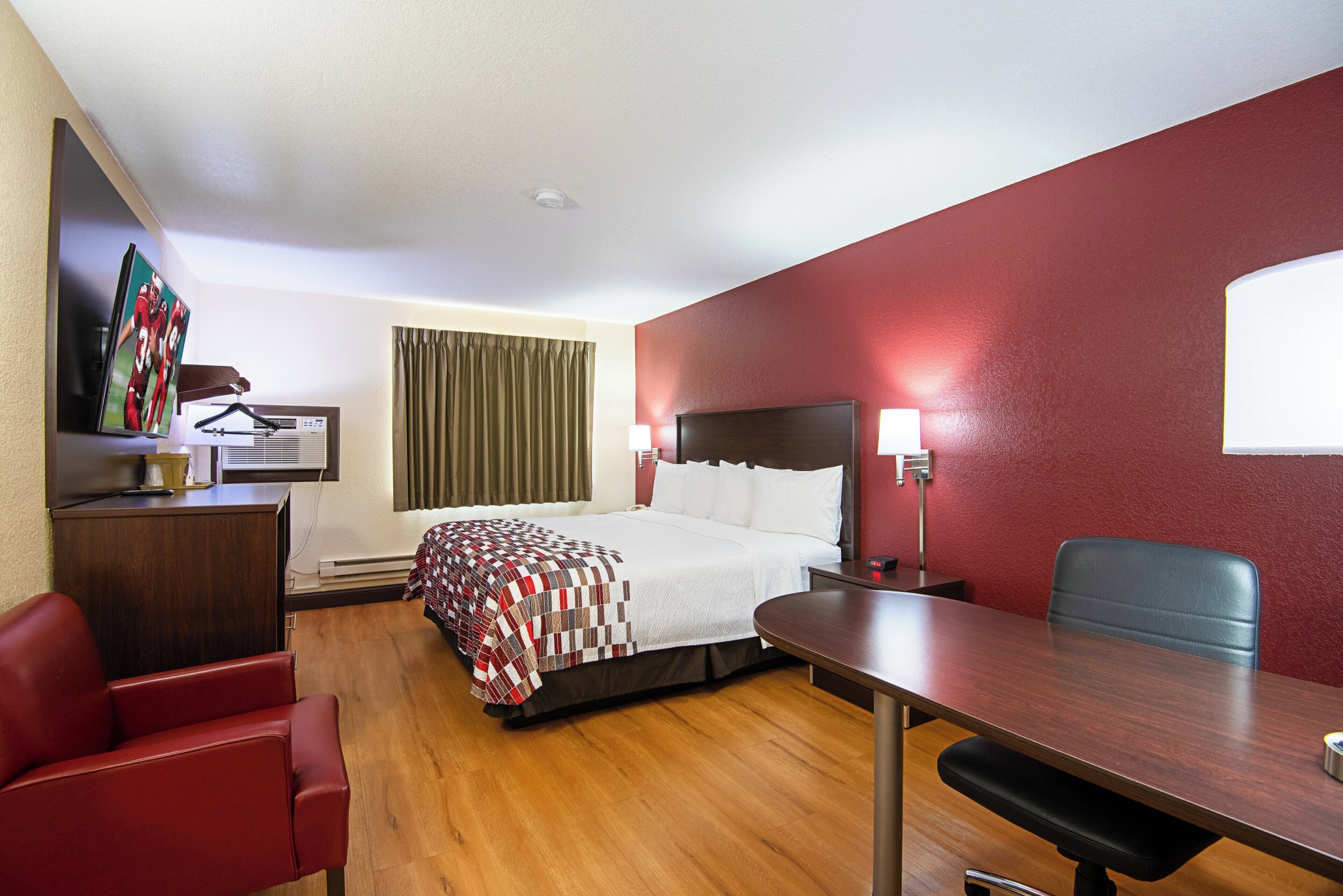 A hotel room with a bed, a desk, a chair, a TV, and a window with curtains.