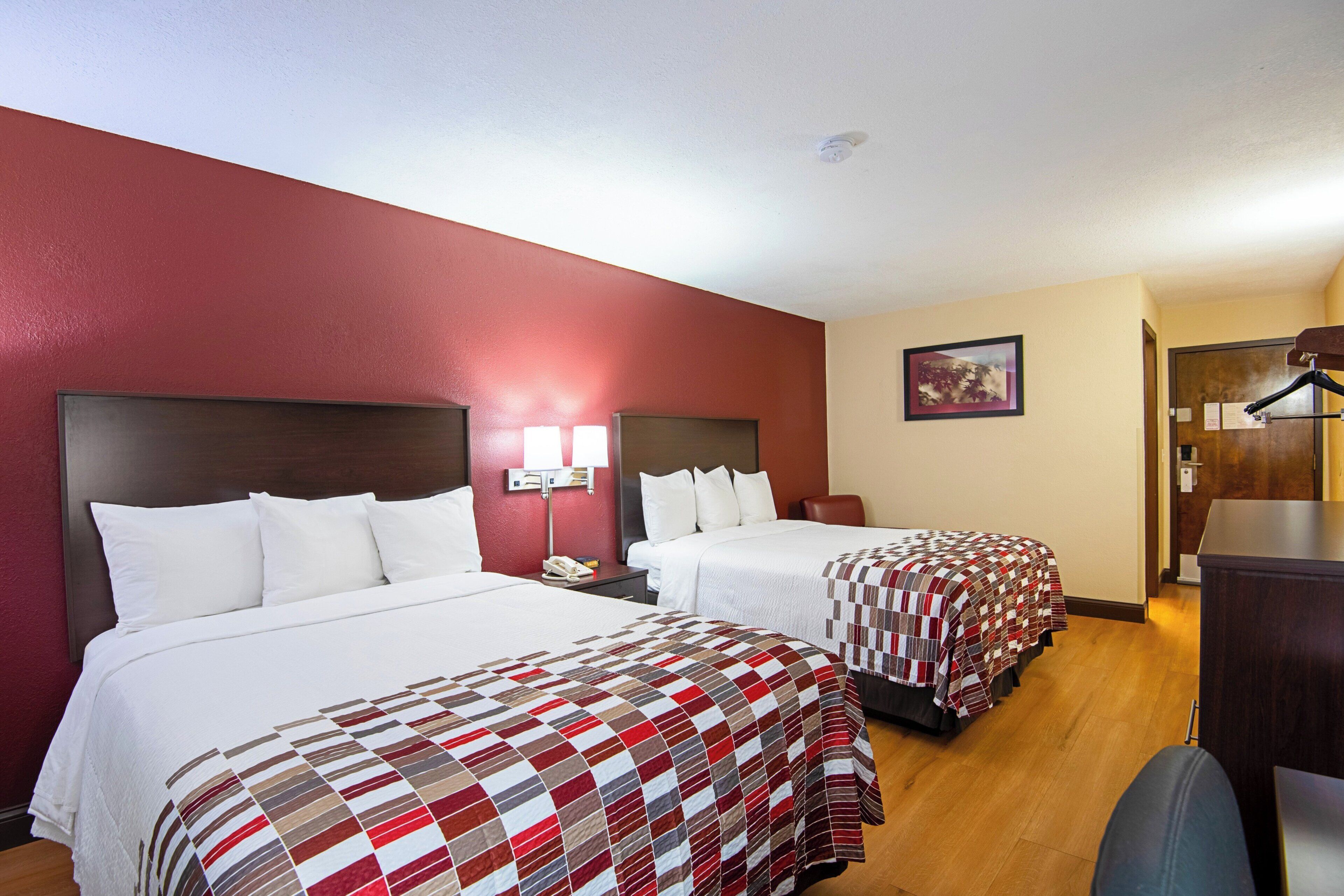 A hotel room with two beds, a desk, a chair, a lamp, and a painting on the wall.