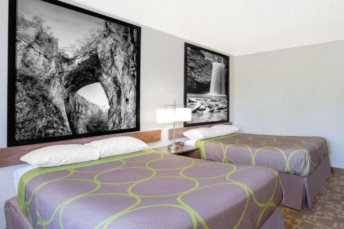 Habitación de hotel con dos camas, una mesita de noche, una lámpara y dos grandes cuadros de paisajes en blanco y negro.