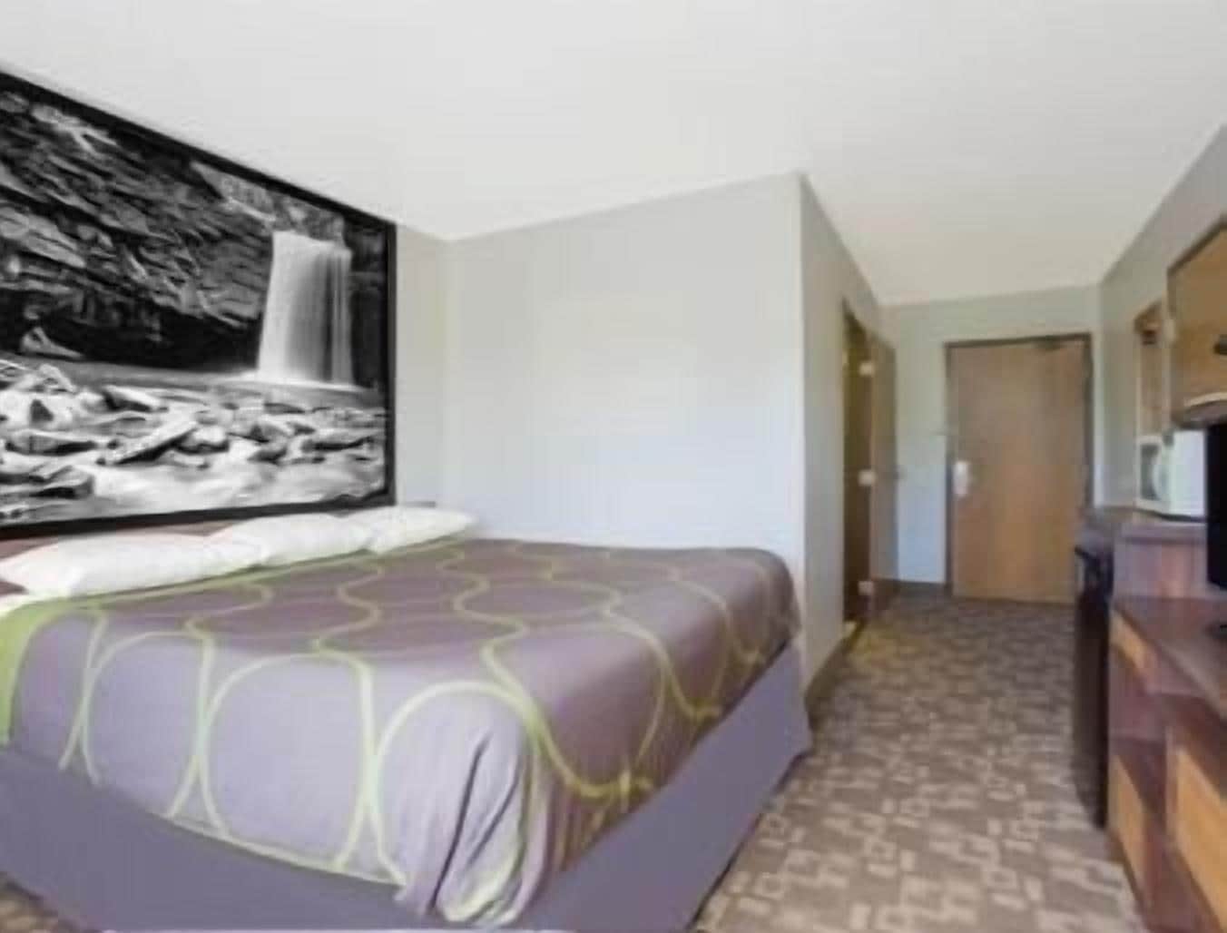 A hotel room with a bed, a large wall-mounted artwork of a waterfall, and a patterned carpet.