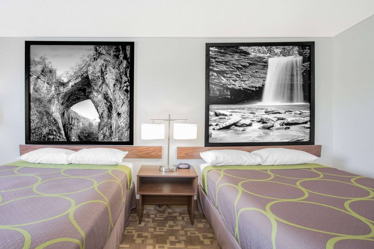 Habitación de hotel con dos camas, cada una con una colcha estampada, una mesita de noche con lámpara y dos fotografías en blanco y negro enmarcadas en la pared.