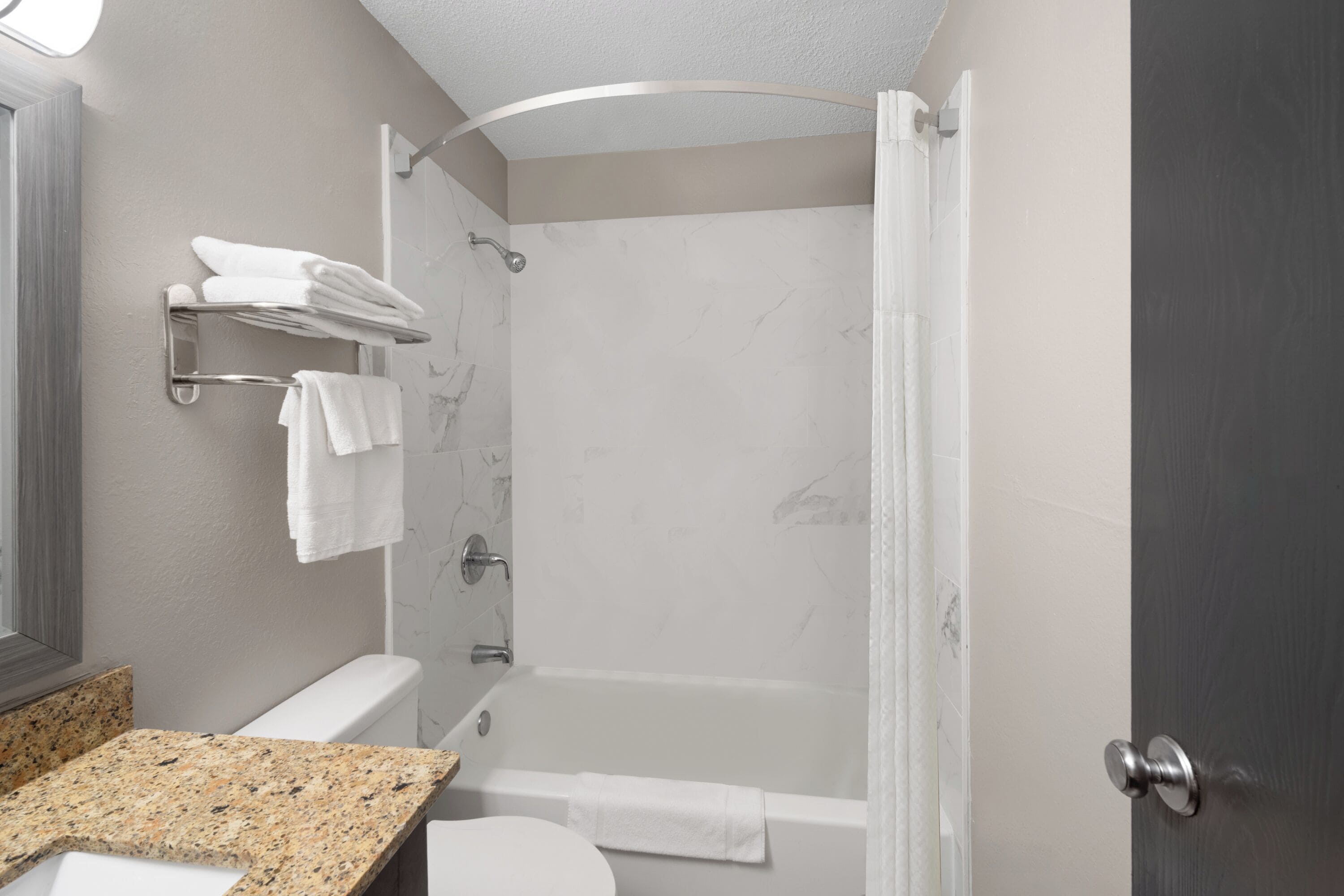 Een moderne badkamer met een granieten aanrechtblad, toilet, douche met glazen deur en een handdoekrek.