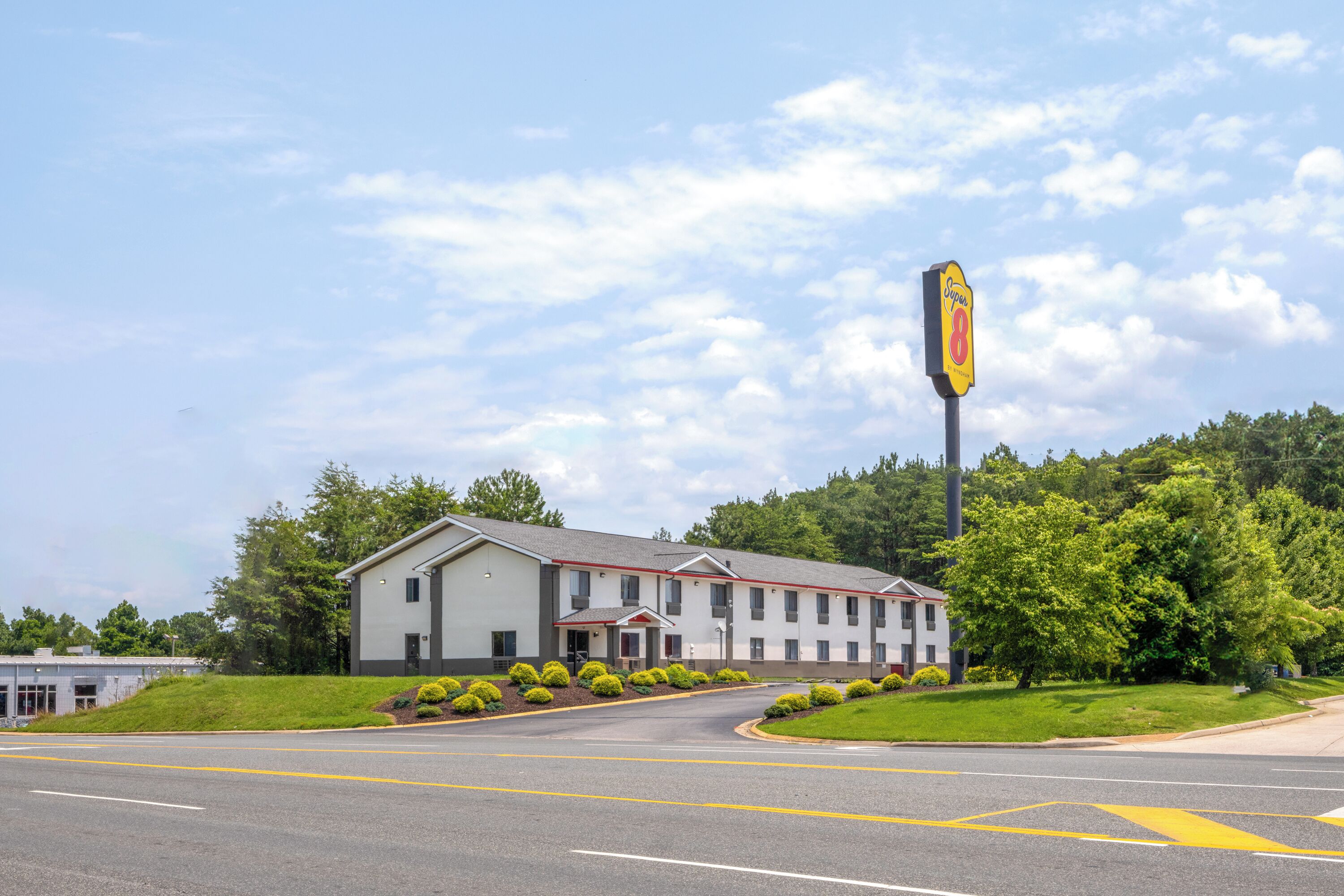 A motel with a large sign, a parking lot, and a building with a red roof.