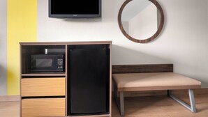 Una habitación pequeña con televisión, microondas, banco y espejo.