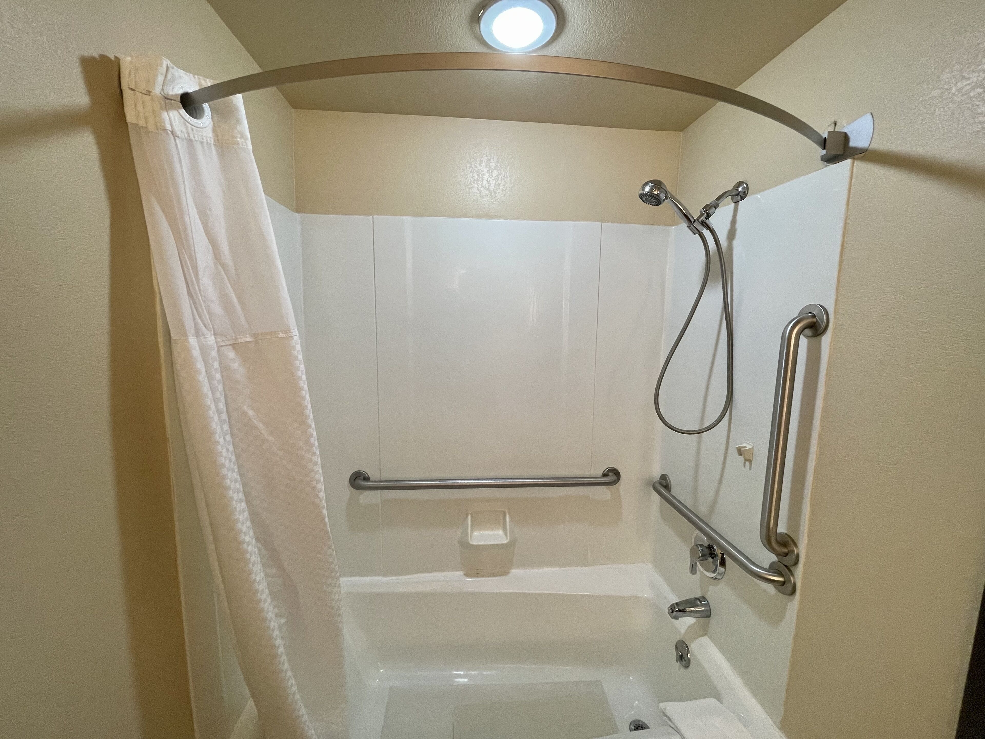 A walk-in shower with a grab bar, a handheld showerhead, and a towel rack.