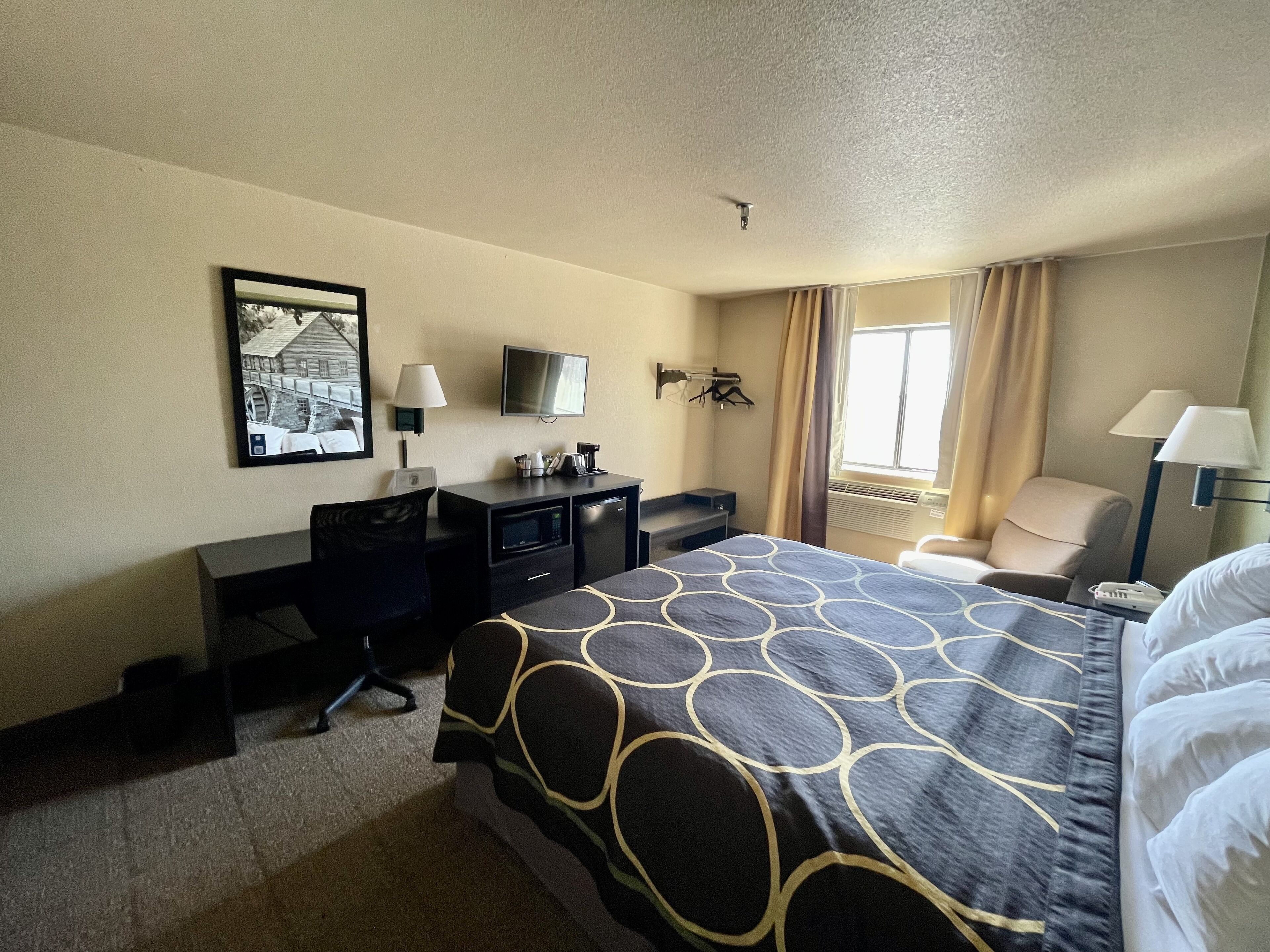 A hotel room with a bed, a desk with a computer, a television, and a window with curtains.