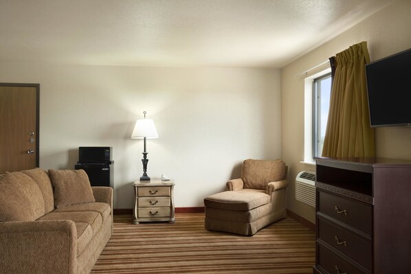 A hotel room with a sofa, armchair, dresser, lamp, TV, and a window with curtains. - Super 8 by Wyndham Macon (Macon)