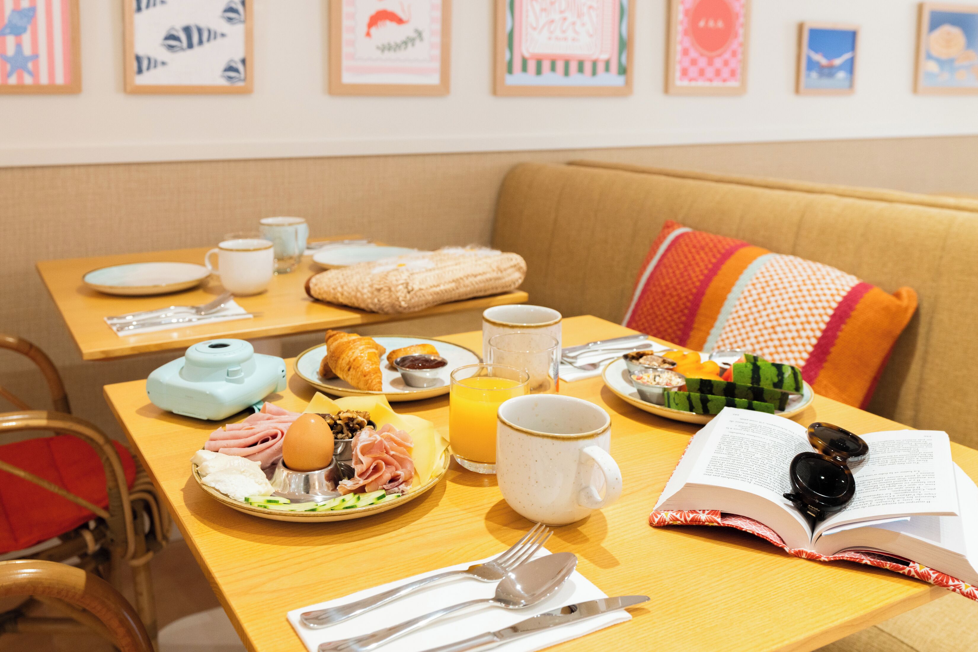 Une table mise pour le petit-déjeuner, avec des assiettes remplies de nourriture, une tasse de café, un livre et une paire de lunettes de soleil.